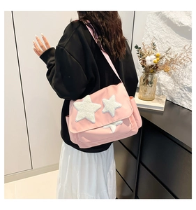 Pink canvas messenger bag with plush star patches shown on model in school style