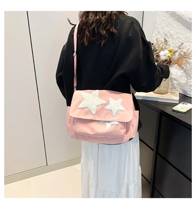 Detail of pink messenger bag featuring white plush star patches and adjustable strap
