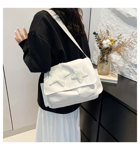 Close-up of white canvas tote bag featuring plush star patches and adjustable shoulder strap