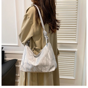 Model wearing a metallic silver hobo bag with unique pleated texture and knot shoulder strap