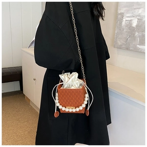 Detail view of textured orange crossbody bag with pearl handle and metal chain strap