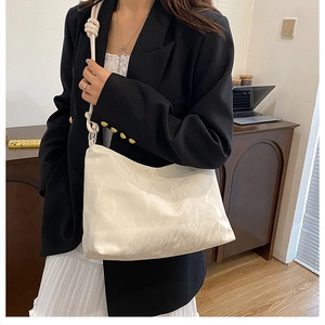 Close-up of beige shoulder bag with knot strap detail on a professional model