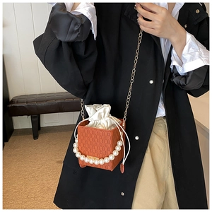 Detail einer braunen Gitter-Eimertasche mit Perlenkapitel und goldener Kettenschulter