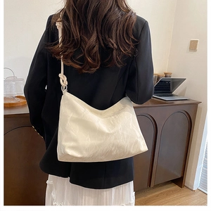 Detail of a cream hobo bag showing knotted shoulder strap and textured faux leather finish