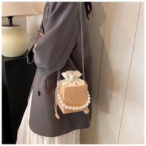 Detail of beige embossed mini bucket bag with pearl handle and gold chain on model