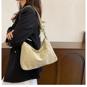 Detail of off-white pleated crescent bag with light green knotted rope strap shown on shoulder