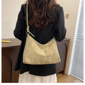 Close-up of pleated beige shoulder bag with knotted strap detail on black blazer