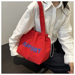Detail of red drawstring canvas tote bag with blue SUPORT lettering and shoulder strap