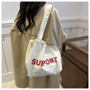 Close-up of cream canvas tote bag with red SUPORT lettering and drawstring closure detail
