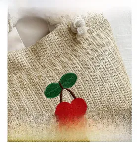 Gros plan sur la texture en paille tressée avec broderie cerise et poignée en coton