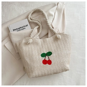 Détail d'un sac cabas en paille tissé avec broderie cerise rouge et anses en corde