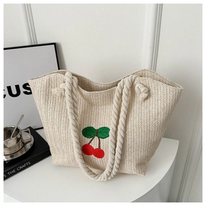 Détail du sac cabas en paille tissée avec broderie cerise et anses en corde beige