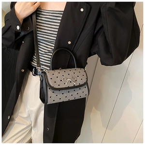 Gray heart pattern handbag with silver bow and black ring handle shown by model