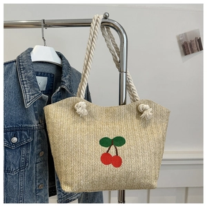 Détail d'un sac en paille avec broderie cerise et poignées en coton blanc