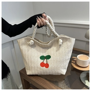 Détail d'un sac cabas en paille tissée avec broderie cerise et anse en corde épaisse