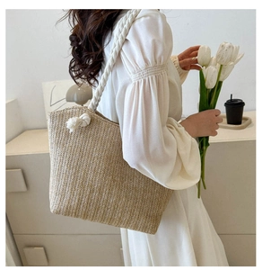Detail of hand-woven straw tote bag featuring white rope handles and decorative knots