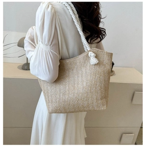 Detail of hand-woven straw tote bag with white cotton rope handle and fringe decor