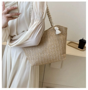 Detail of hand-woven straw tote bag with chunky cotton rope handles and decorative tassels