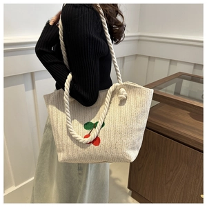 Détail d'un sac cabas en paille avec broderie cerise et poignées en corde tressée