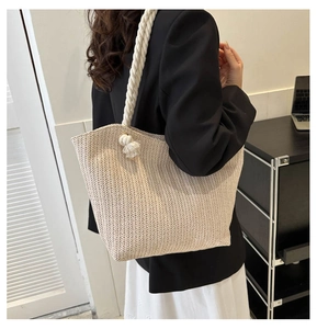 Close-up of a woven straw tote bag with rope handles worn over a black blazer