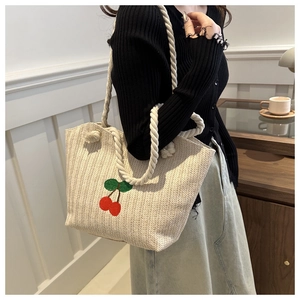 Détail d'un sac cabas en paille tissée avec broderie cerise et anses en corde blanche