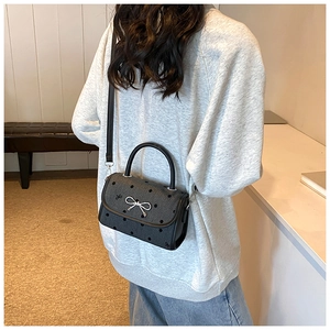 Close-up of black polka dot shoulder bag with silver metallic bow buckle on model