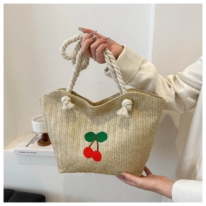 Détail d'un sac en paille tissée avec cerises rouges brodées et poignée en corde de coton blanc