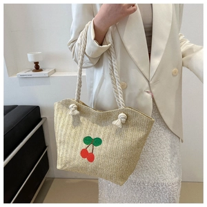 Détail d'un sac en paille avec broderie cerise rouge et poignées en corde de coton