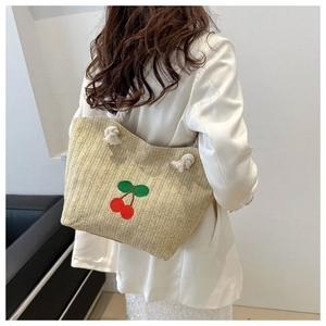 Détail d'un sac cabas en paille tissée avec broderie cerise et anses en corde blanche