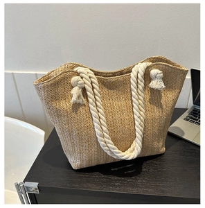 Detail of hand-woven straw tote bag featuring thick white rope handles with tassel accents
