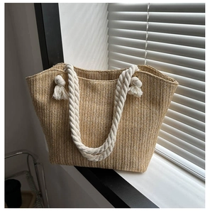 Detail of straw tote bag with white cotton rope handles and gold grommets on window sill