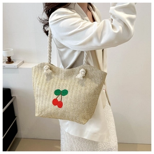 Sac fourre-tout en paille brodé de cerises présenté par un mannequin avec des anses en corde