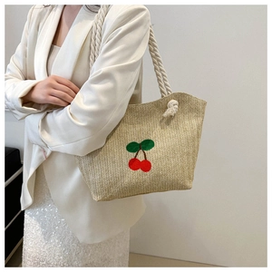 Détail d'un sac cabas en paille tissée avec broderie cerise et anse en corde sur l'épaule