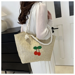 Détail d'un sac cabas en paille tissée avec cerises brodées et anses en corde épaisse