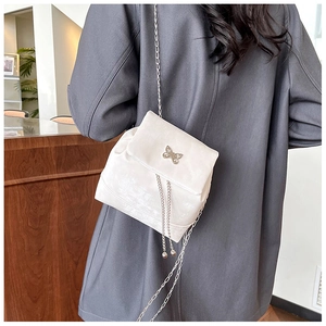 Detail of cream white velvet crossbody bag with metallic bow and chain on a model