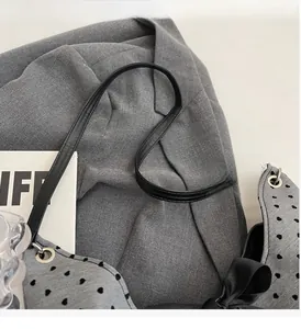 Detail of grey tote bag with heart patterns, featuring a large black silk bow and leather strap