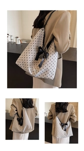 Detail of knit tote bag featuring black heart patterns and a large decorative ribbon bow