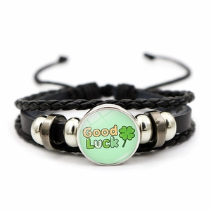 Macro detail of Good Luck green clover charm and braided black leather bracelet