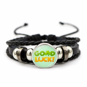 Close-up of leather bracelet featuring a GOOD LUCK glass dome and braided cord details