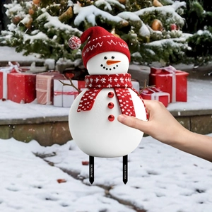Close-up of a snowman garden stake with red knitted hat and scarf in snowy background