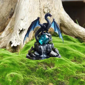 Close-up of a fantasy black dragon figurine with blue wings and a crystal ball on a mossy rock