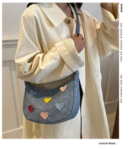Close-up of blue denim hobo bag with colorful heart patches on a neutral background