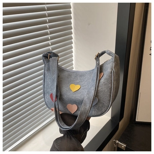 Detail of blue denim heart crescent bag with multi-colored patches and wide strap