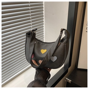Macro view of dark grey crescent shoulder bag with colorful heart patches and wide strap