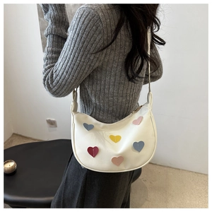 Détail du sac bandoulière demi-lune crème avec patchs cœurs colorés sur un mannequin