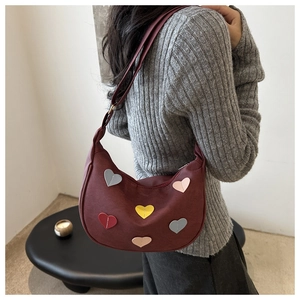 Détail d'un sac demi-lune bordeaux avec écussons cœur colorés porté par un mannequin