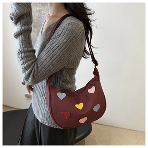 Détail d'un sac demi-lune bordeaux avec écussons cœurs colorés porté par un mannequin