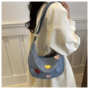 Détail du sac hobo en jean bleu avec patchs de cœur colorés porté à l'épaule