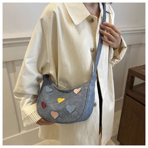 Détail d'un sac demi-lune gris avec des écussons cœurs colorés porté par un mannequin