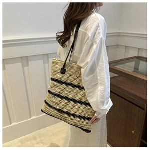 Detail of striped straw tote bag with black leather shoulder straps on model